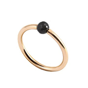 A minimalist yellow gold ring featuring a single, small, round black faceted diamond, shown on a plain white background.