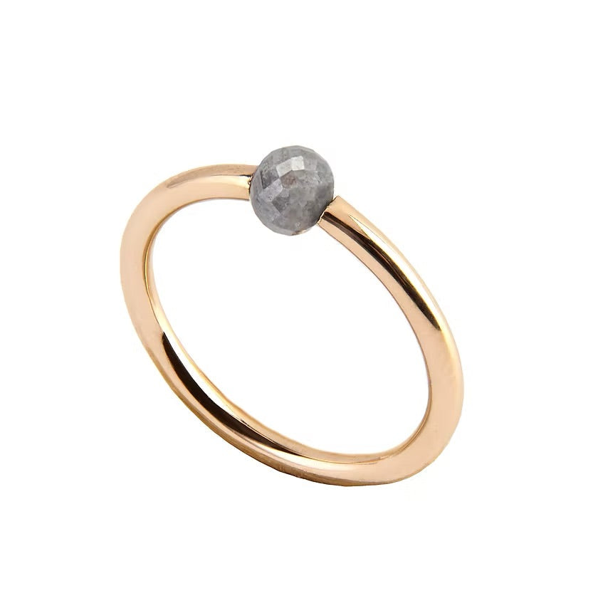 A minimalist yellow gold ring featuring a single, small, round grey faceted diamond, shown on a plain white background.