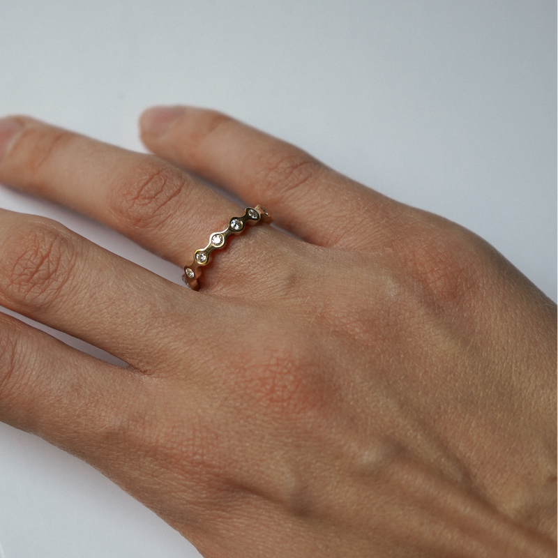 A close-up of a person's hand wearing a delicate gold ring with small round-cut diamonds.