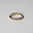 A gold eternity-style ring with a wavy, scalloped edge and small clear gemstones set along the front, photographed on a clean light gray background.