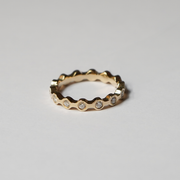 A gold eternity-style ring with a wavy, scalloped edge and small clear gemstones set along the front, photographed on a clean light gray background.