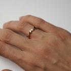 A close-up of a person's hand wearing a delicate gold ring adorned with small diamonds, resting on a white surface.