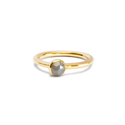 A delicate gold ring with a small, round, pale grey diamond in a bezel setting, shown on a plain white background.