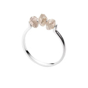 A white gold ring featuring three small, raw-cut diamond stones set across the top, shown against a plain white background.