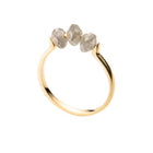 A gold ring featuring three small, raw-cut diamond stones set across the top, shown against a plain white background.