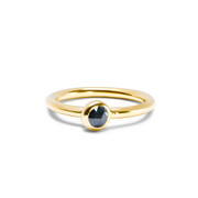 A yellow gold ring with a single faceted dark ocean blue gemstone in a bezel setting, shown on a clean white background.