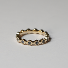 A gold eternity ring with a wavy, scalloped edge and small round blue sapphires set along the band, photographed on a neutral light gray background.