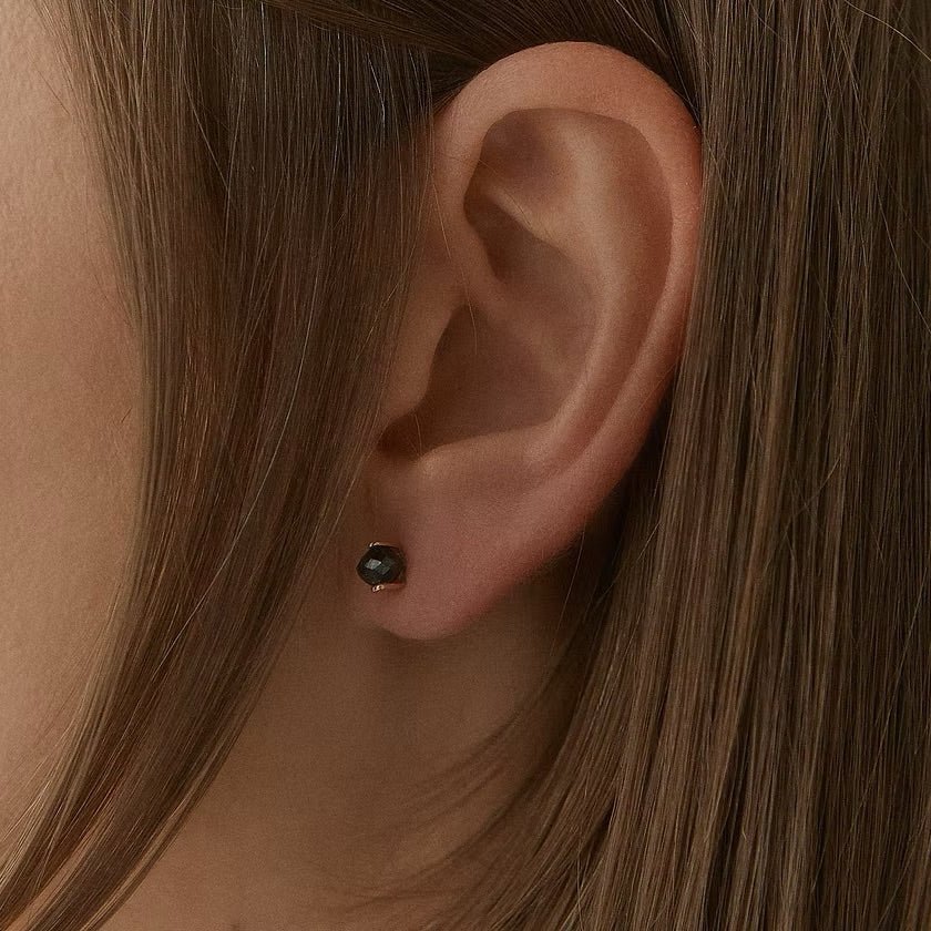 Close-up of a person's ear wearing a yellow gold & black diamonds stud earring, against brown hair.