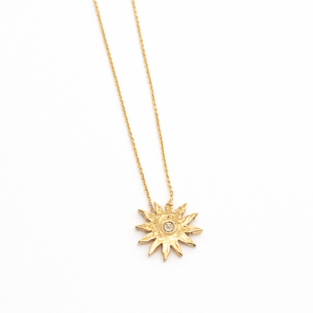 Gold sun-shaped pendant necklace on a white background