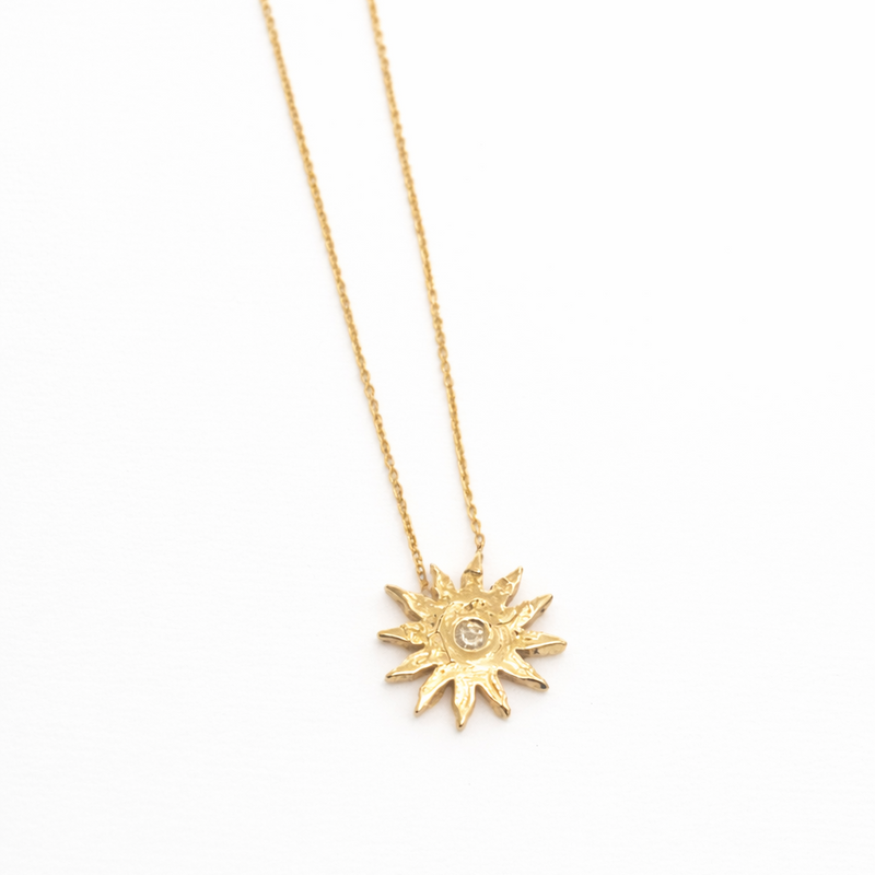Gold sun-shaped pendant necklace on a white background