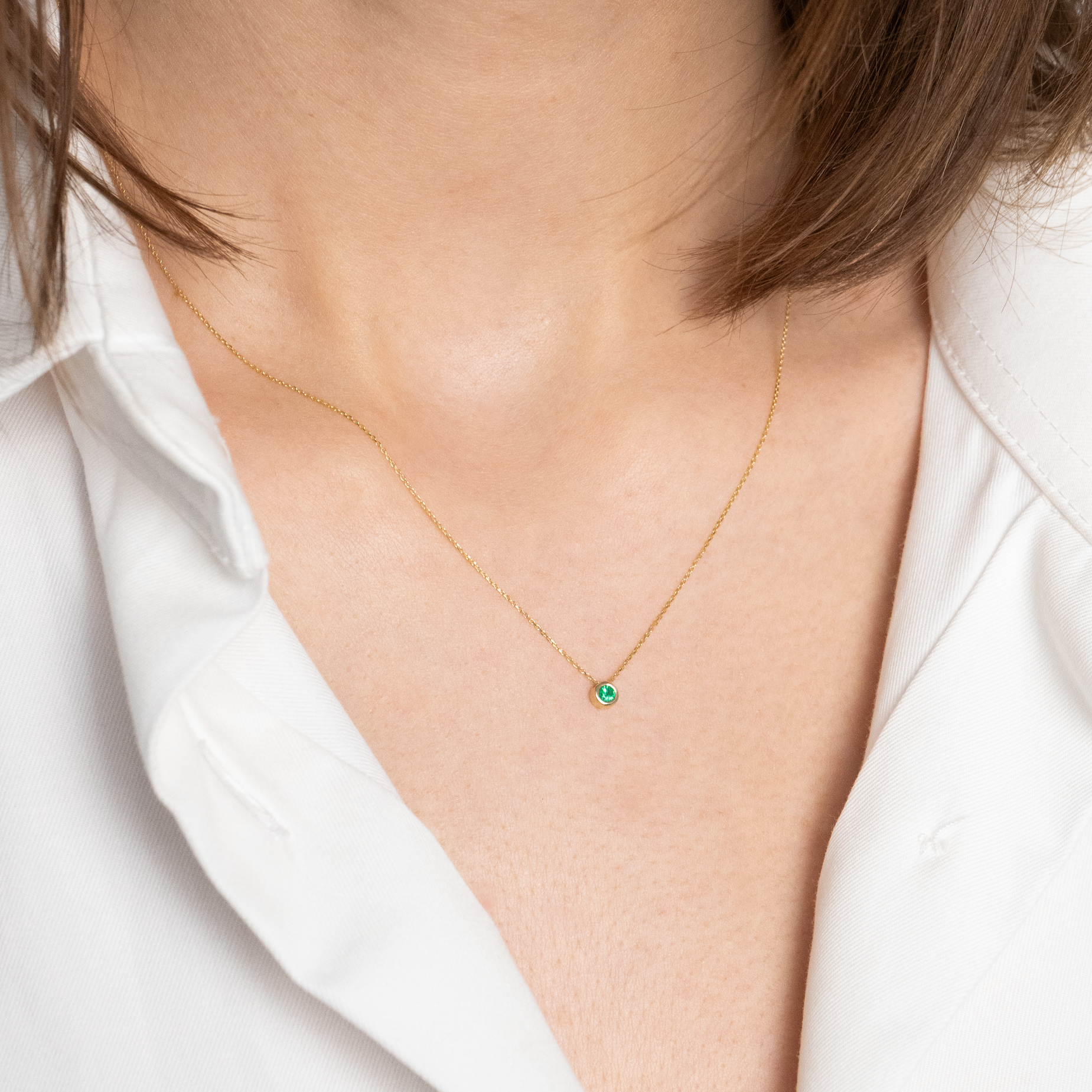 Woman wearing a yellow gold necklace with emerald pendant.
