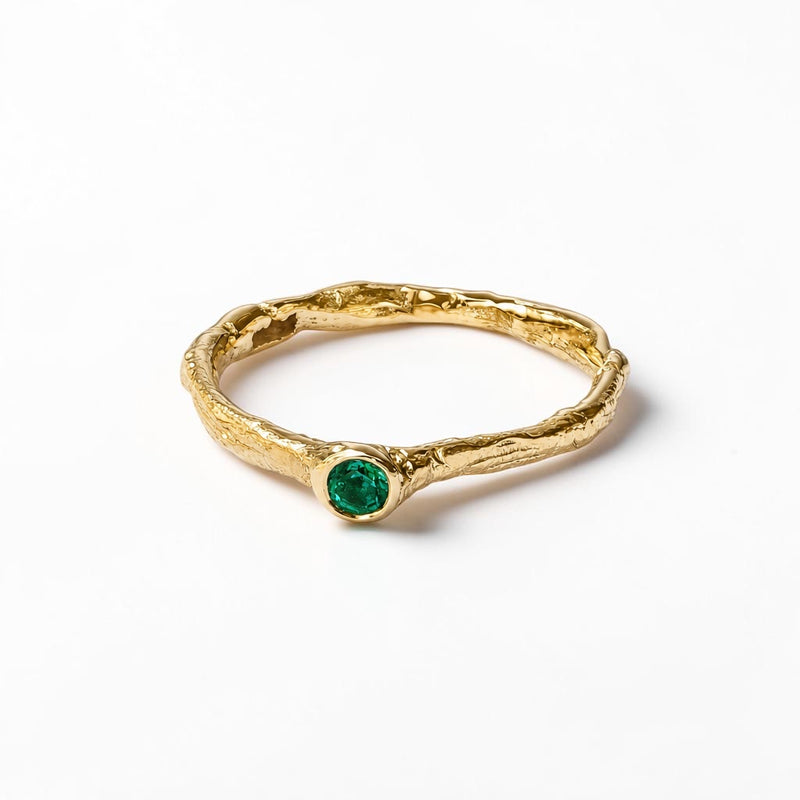 Gold ring with a green emerald gemstone on a white background