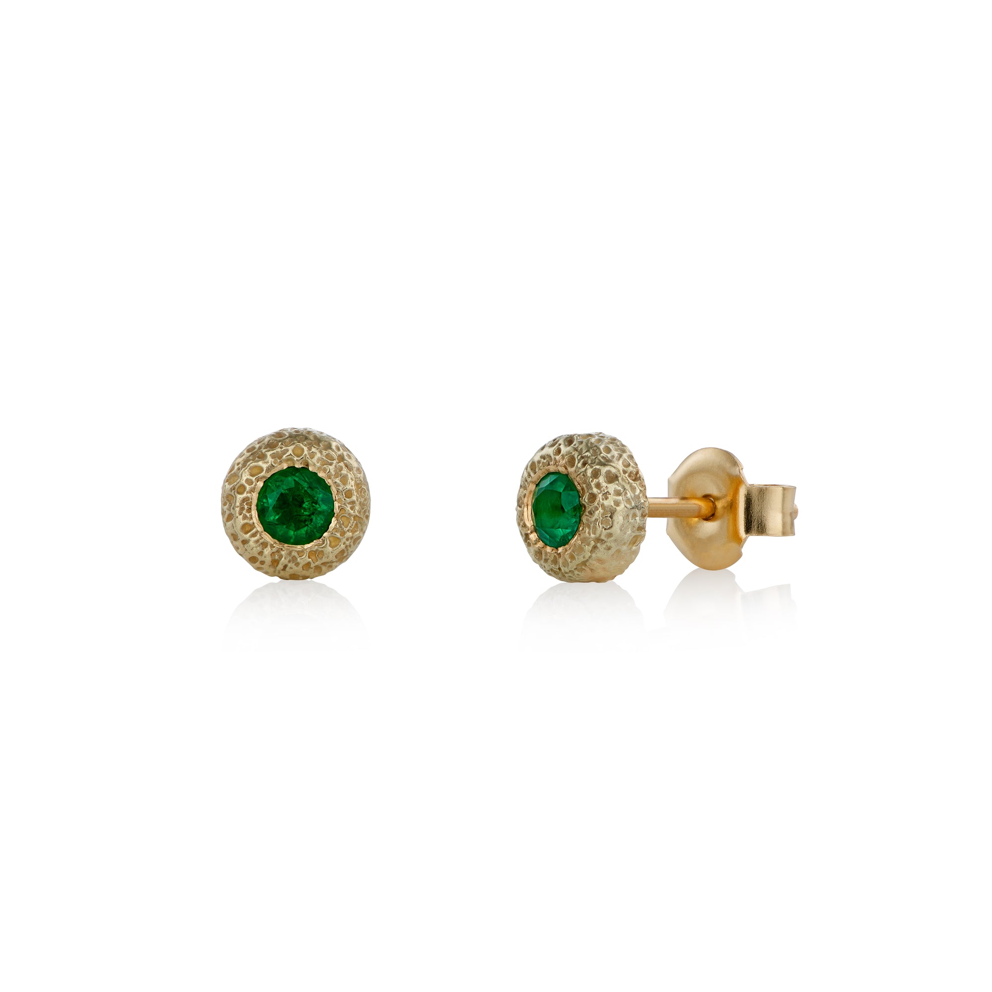 Round stud earrings in textured yellow gold, each set with a single emerald in a bezel setting. 