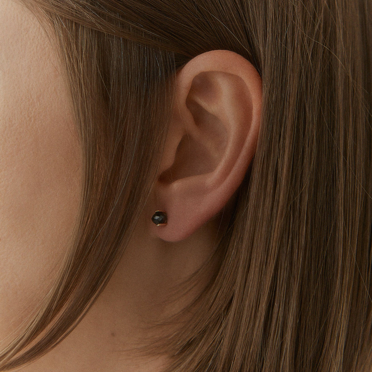 A pair of gold stud earrings with faceted gray diamonds in a prong setting, shown on a clean white background.