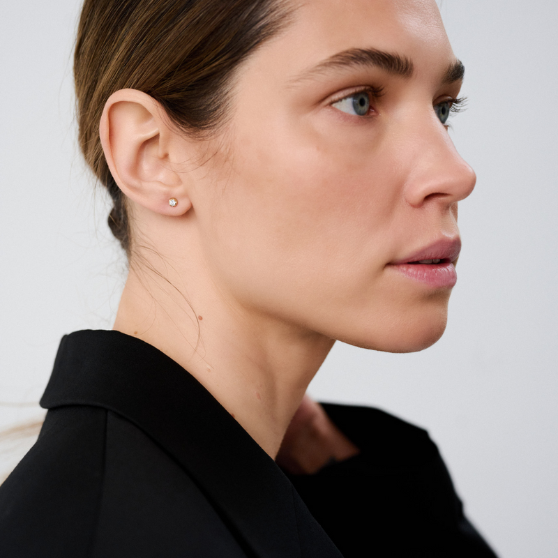 Woman wearing stud earrings featuring round brilliant-cut diamonds set in 14k yellow gold.