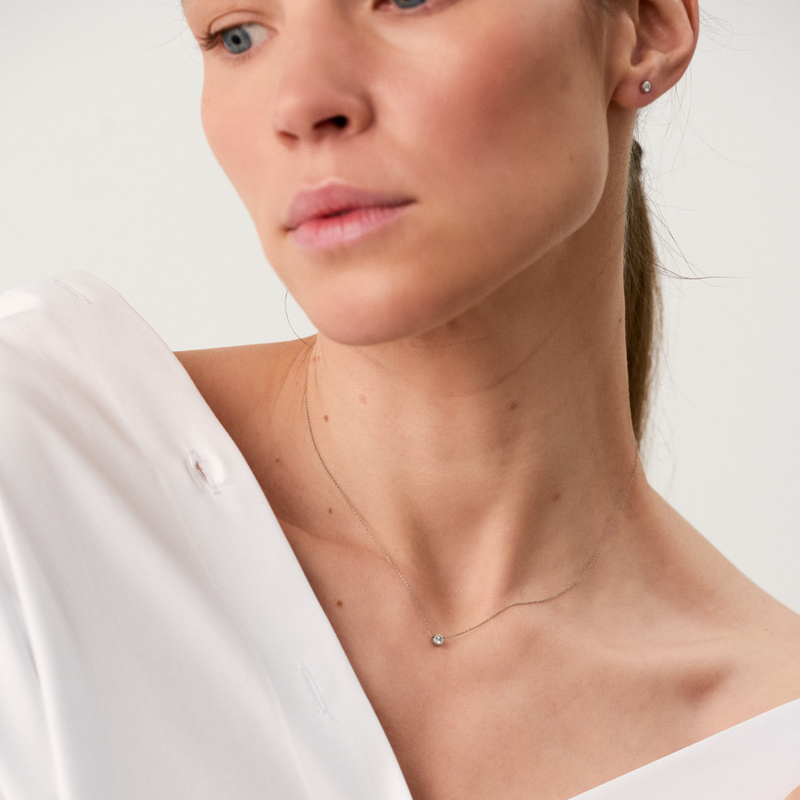 Woman wearing white gold pendant featuring a round brilliant-cut diamond, suspended from a delicate gold chain.