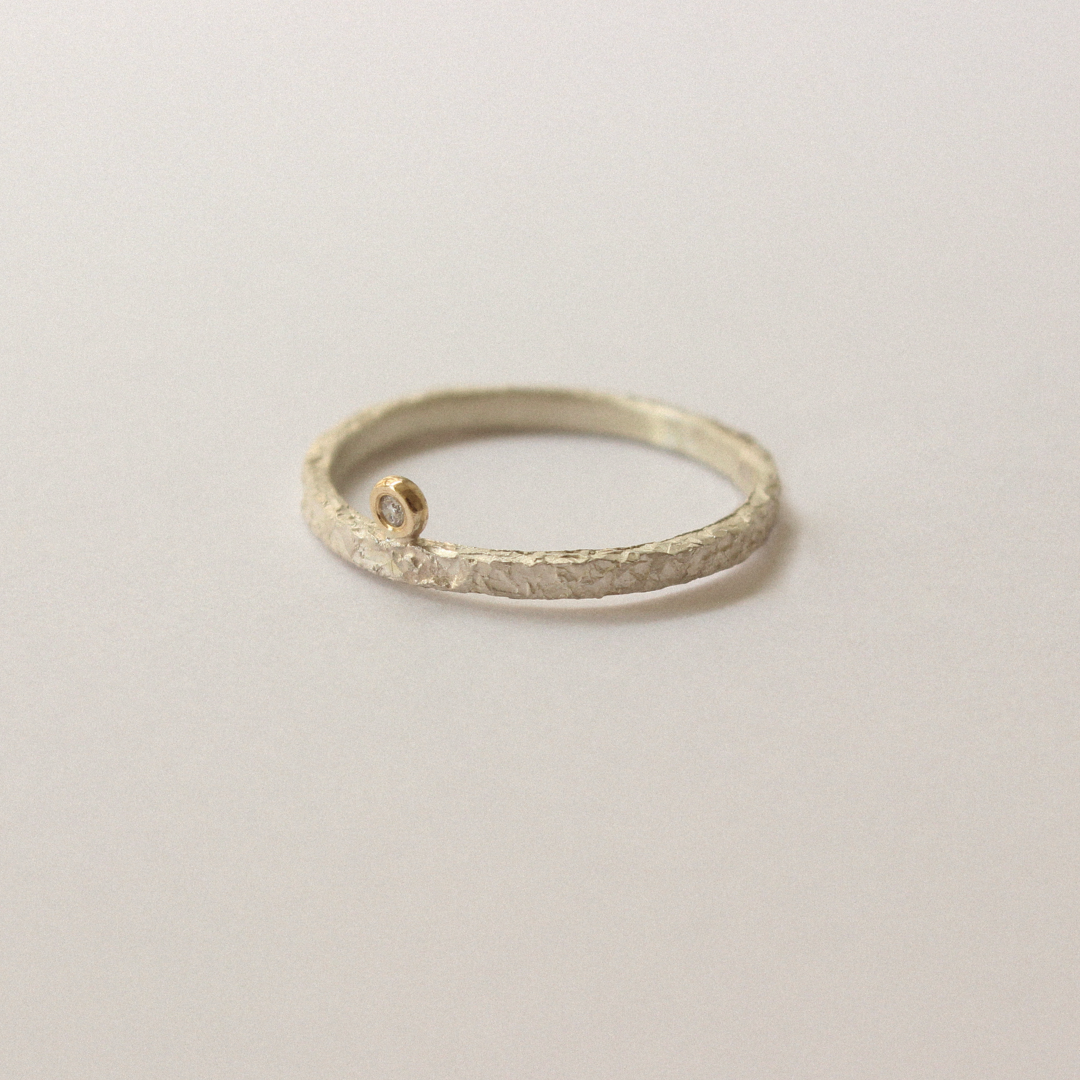 Silver ring with textured band and small diamond on a light gray background