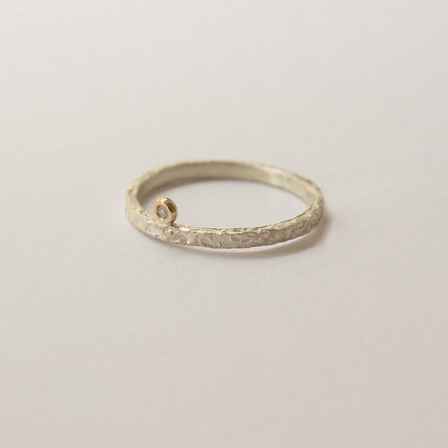 Silver ring with textured band and small diamond on a light gray background