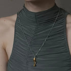 Woman wearing a green dress with a necklace featuring a gold pendant against a neutral background