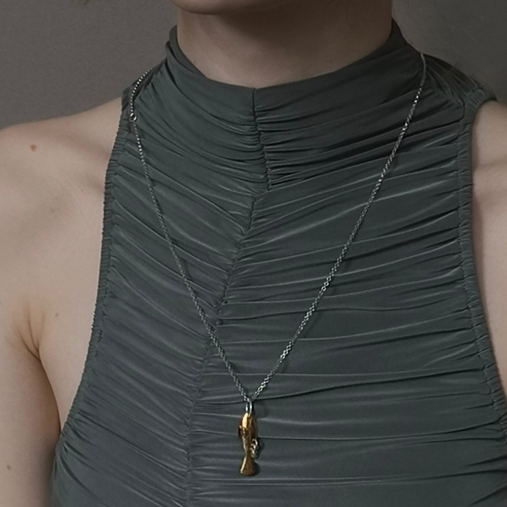 Woman wearing a green dress with a necklace featuring a gold pendant against a neutral background