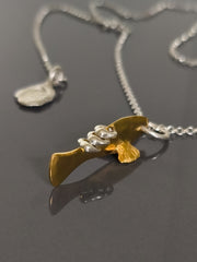 Gold and silver fish pendant on a chain against a gray background