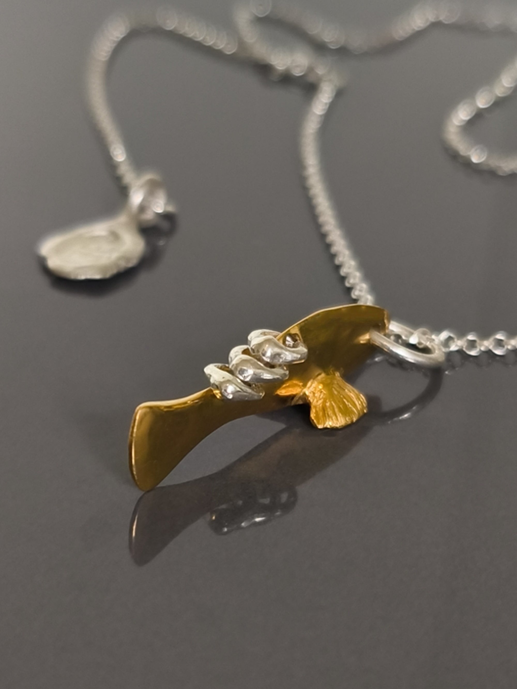 Gold and silver fish pendant on a chain against a gray background