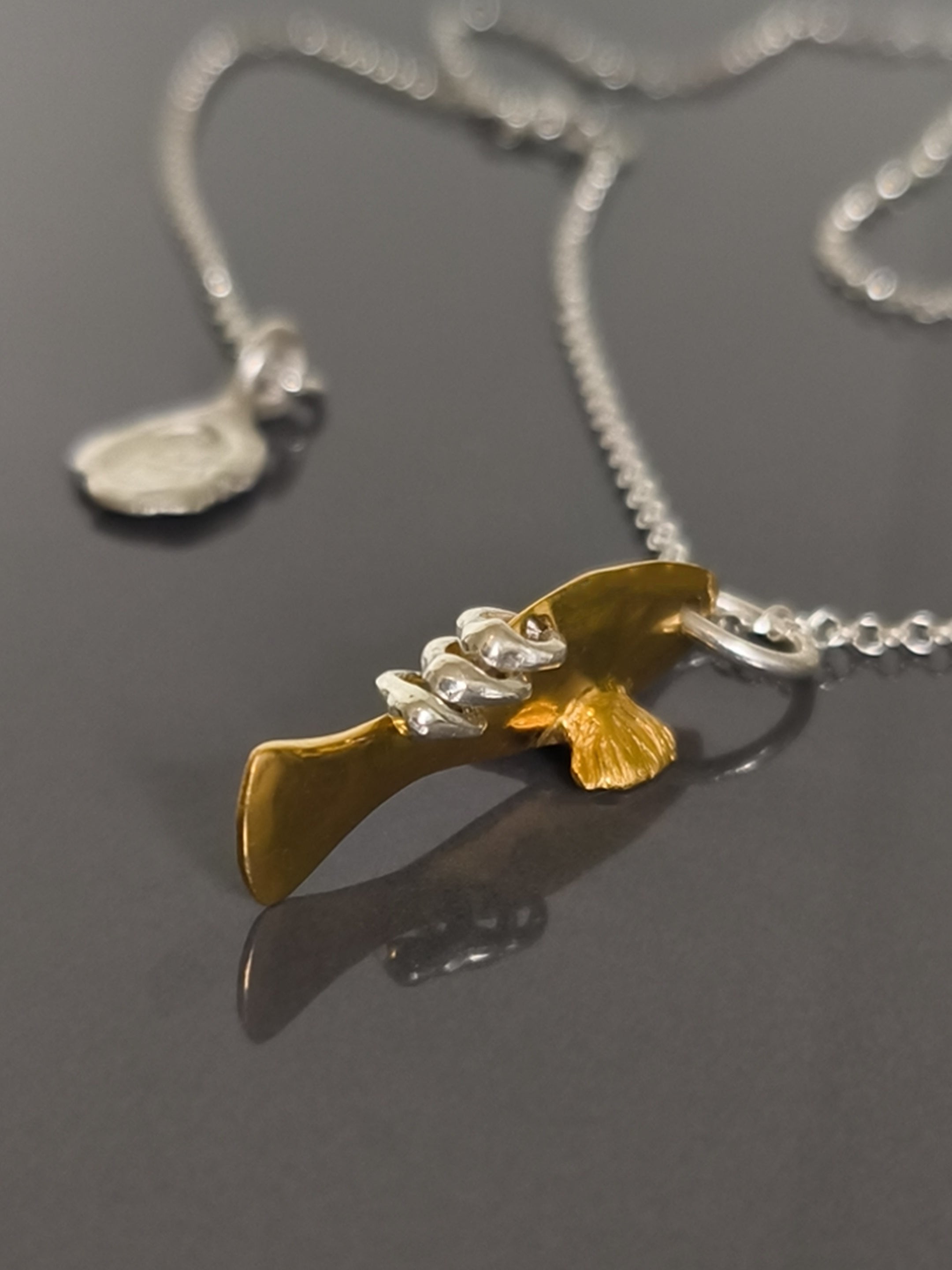 Gold and silver fish pendant on a chain against a gray background
