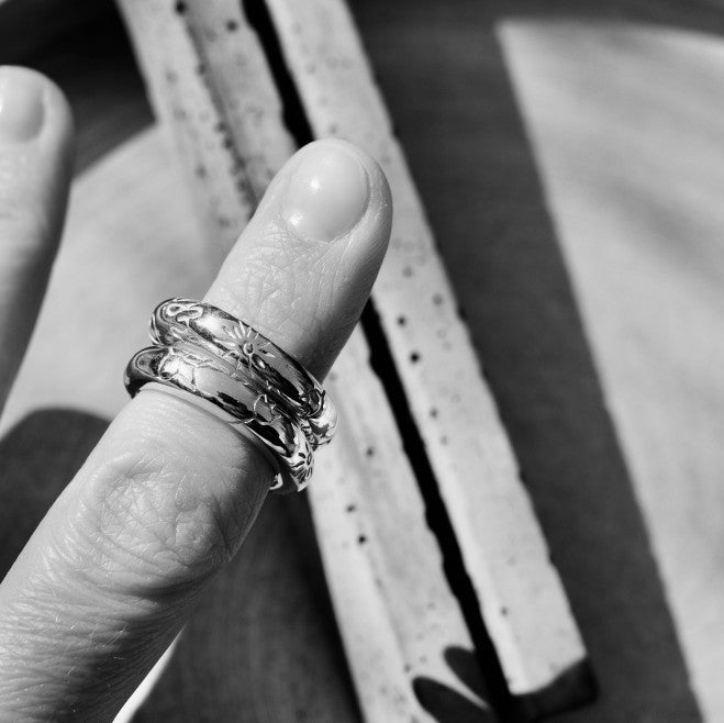 Two polished silver rings with engraved patterns on finger.