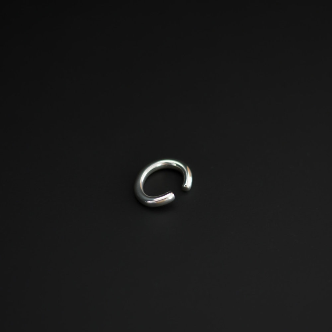 A polished silver-toned metal open-ended ring ear cuff, shown on a plain black background.