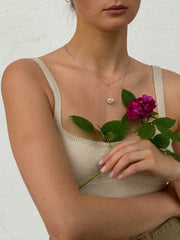 Woman wearing two minimal design yellow gold necklaces. One is with diamond, the other is with baroque pearl.