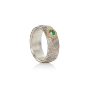 A silver ring with a central emerald and gold detailing, presented against a white background.
