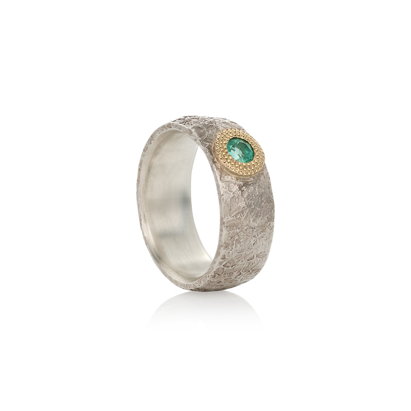 A silver ring with a central emerald and gold detailing, presented against a white background.