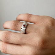 A silver ring with an orange sapphire set in the center, adorned with gold details, displayed on a person's finger.