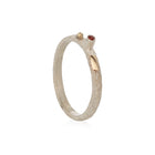 A narrow silver ring with a orange sapphire in the center and gold bubbles around it.