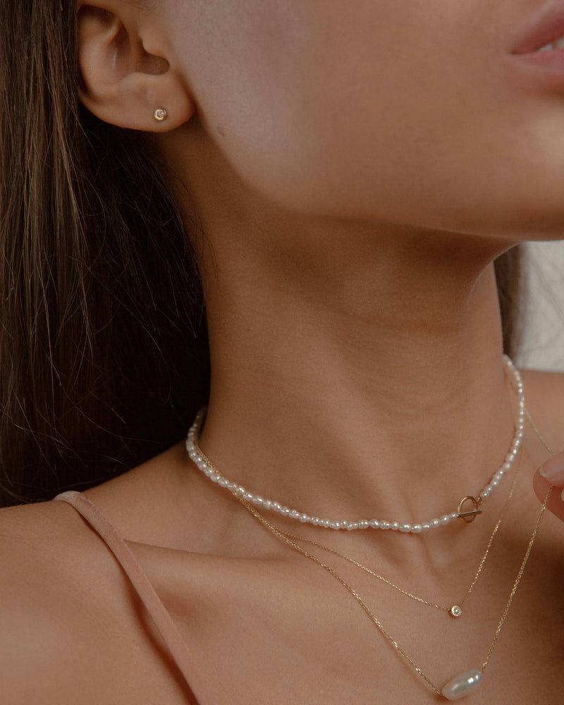 Woman wearing three minimal design yellow gold, pearls and diamonds necklaces.